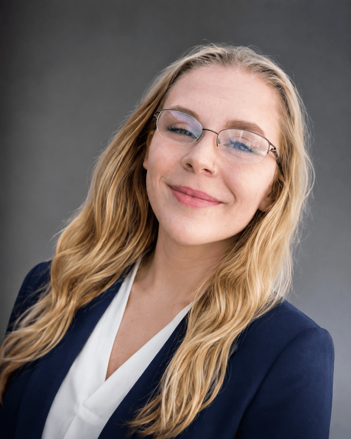 Professional headshot of a blonde woman with glasses wearing a navy blazer and white shirt.