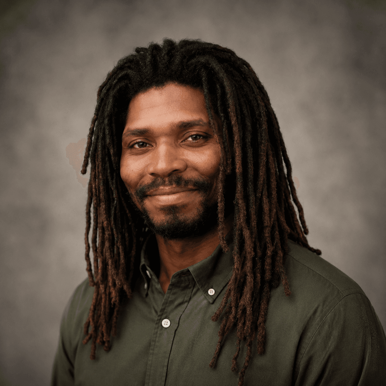 Smiling Black man with long dreadlocks and a beard wearing a green button-down shirt.
