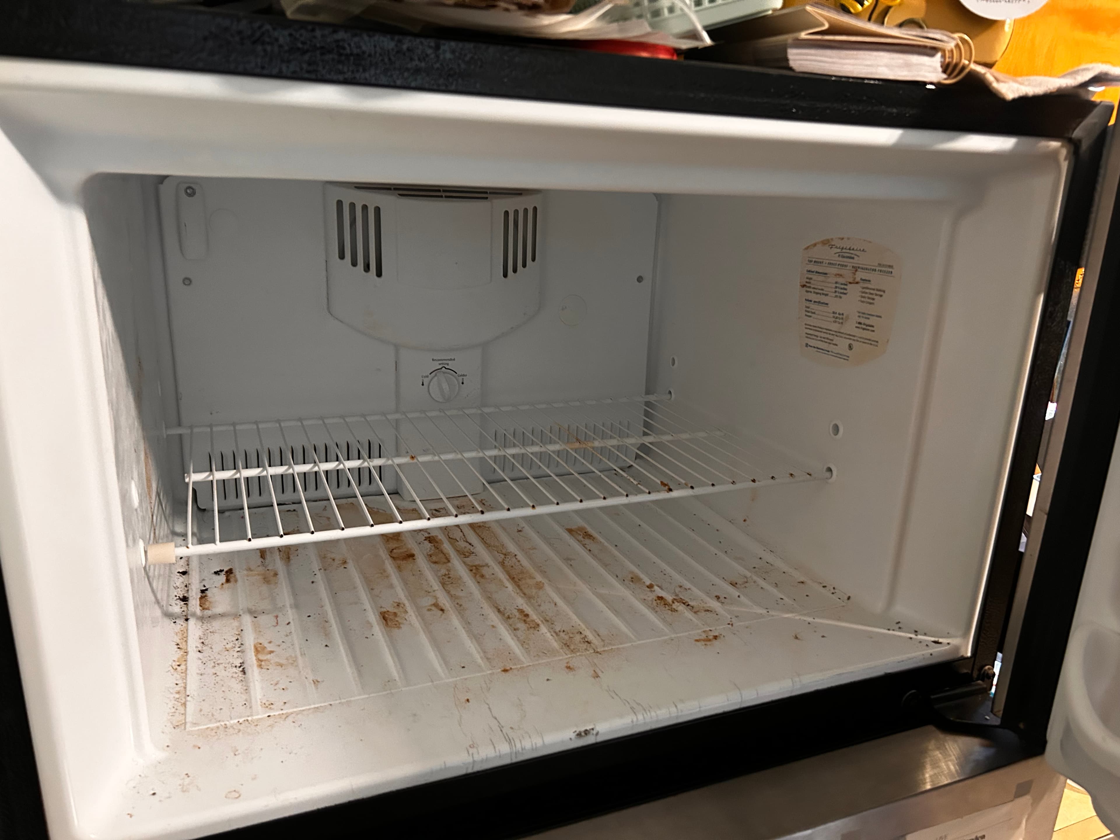 Dirty, empty freezer compartment with brown stains on the bottom and a wire rack.