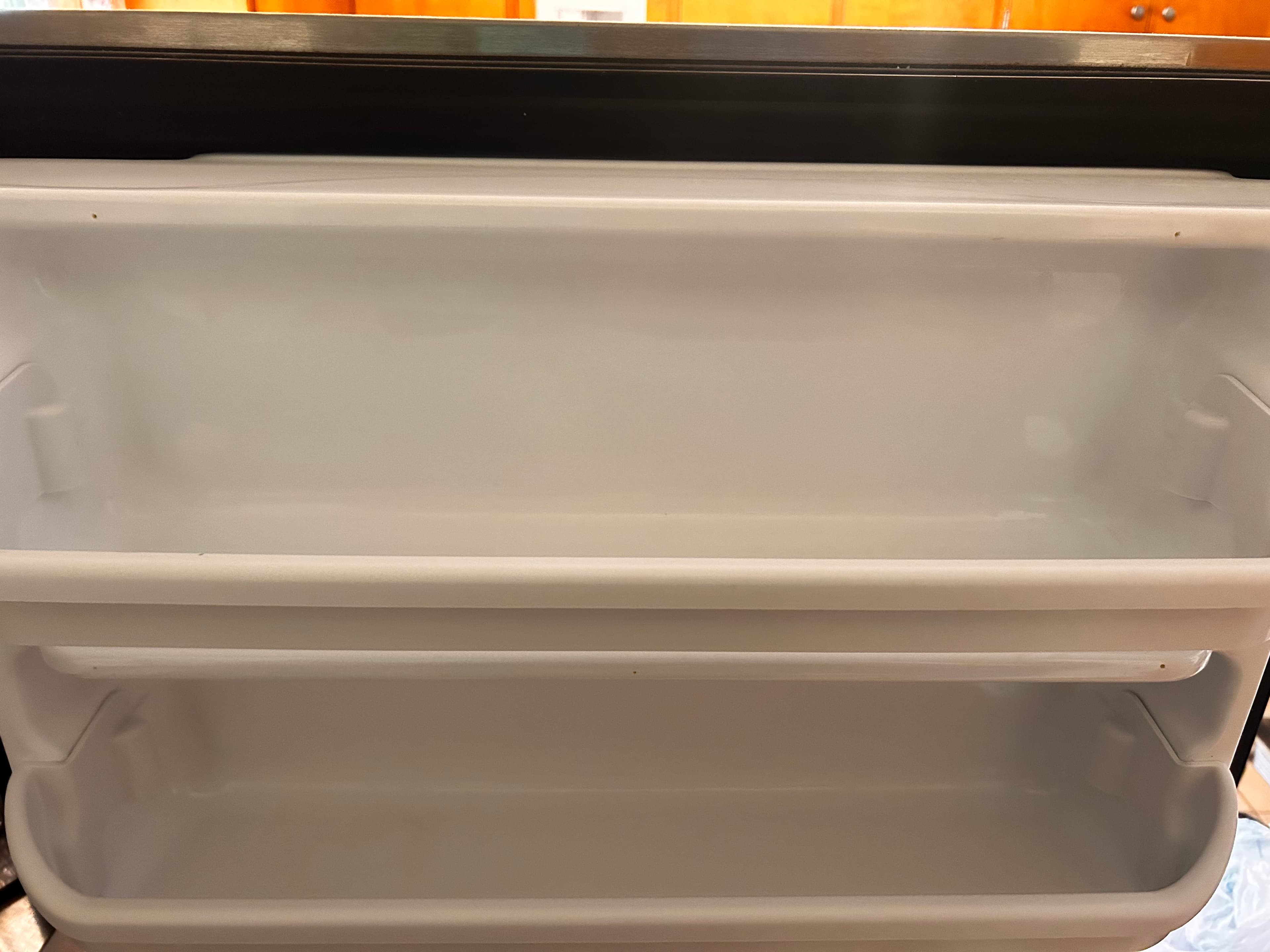 Two empty, clean white plastic shelves inside a refrigerator door, showing a close-up perspective.