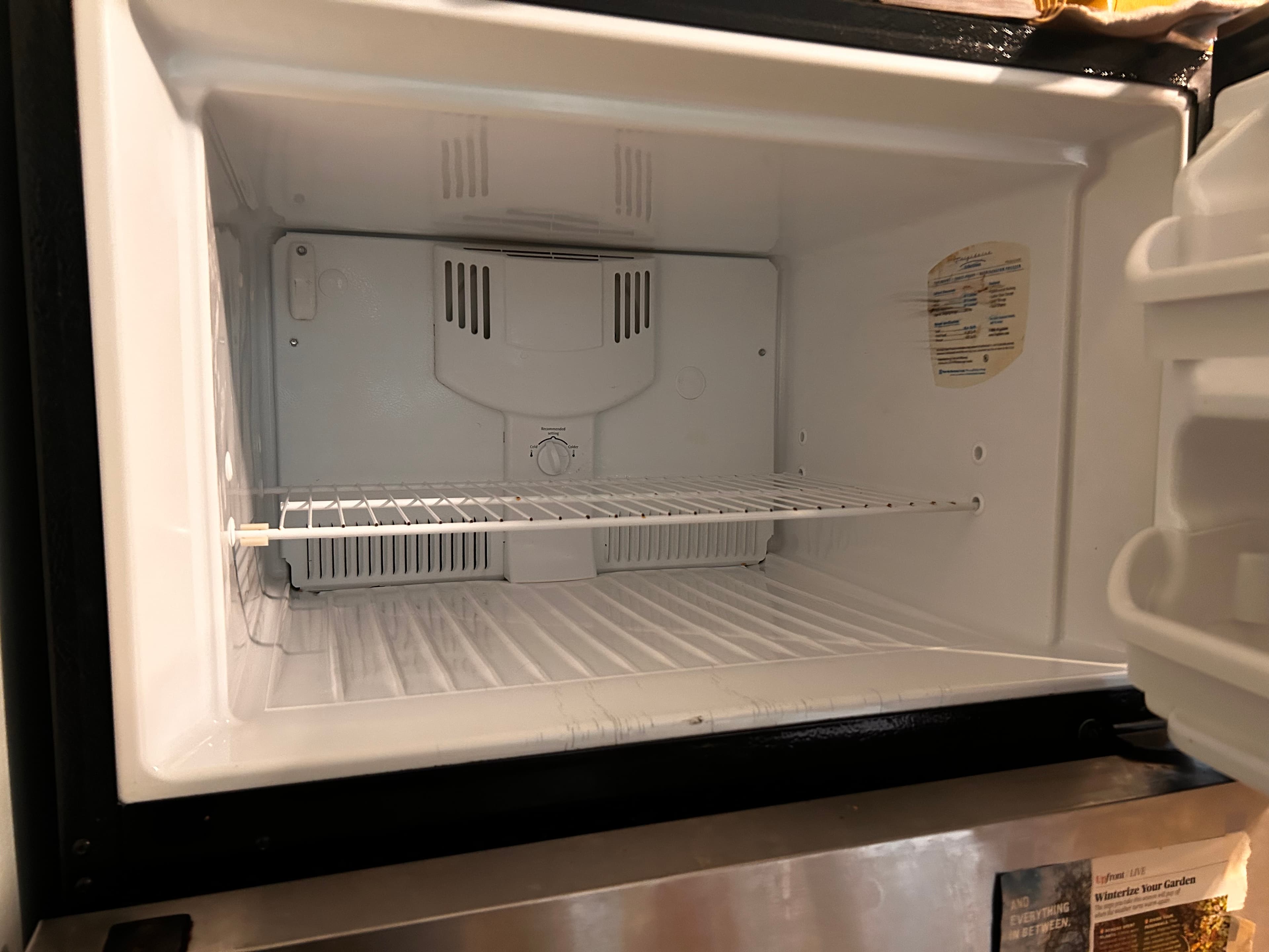 Empty white freezer compartment featuring a wire shelf and a central temperature control dial.